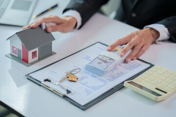 The real estate agent gives the buyer the house keys on a table with modern miniature house model.