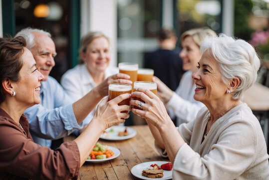 Group of senior friends raising beer glasses in a toast, enjoying a meal together at a restaurant