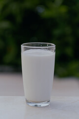Glass of milk on the white ceramics floor with blurred nature background. Vertical.