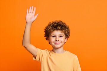 Side profile of a young boy waving hello to friends, isolated on an orange background