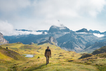 A solitary hiker ventures forth to explore a breathtaking and majestic mountain landscape beneath a...