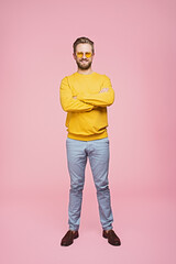 Smiling man in yellow clothing, including sweater and sunglasses, posing with arms crossed in...
