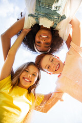 Three happy friends are huddled together from a low angle while outside on a sunny day, sharing...