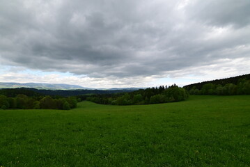 Breathtaking Czech mountain landscape at sunset, with glowing green meadows, forested hills, and distant peaks bathed in warm light. A peaceful and untouched view of the Czech countryside, showcasing 