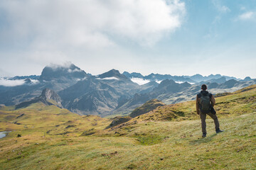 A lone explorer stands still, gazing in awe upon the breathtaking mountain scenery beneath a bright...