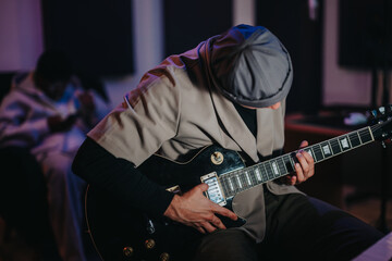 A musician intensely plays an electric guitar in a dimly lit recording studio, creating music. The...