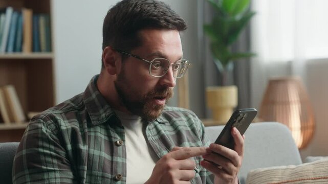 Portrait adult man looking at mobile phone shock reaction amazed bad news close mouth with hand problem online indoors. Closeup male in apartment holding use smartphone shocked reaction at home scared