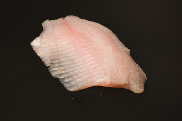 Fresh tilapia fillet on black background, top view.
