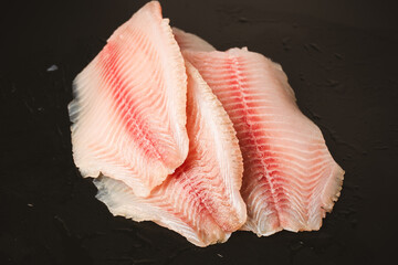 Fresh tilapia fillet on black background, top view.