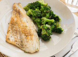 Fried fillet of sea bass with garnish of broccoli on black warm stone plate