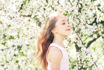 Fototapeta premium Young girl enjoying a peaceful childhood moment among blooming white cherry blossoms in a spring garden