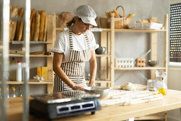 Elderly woman baker rolls out dough