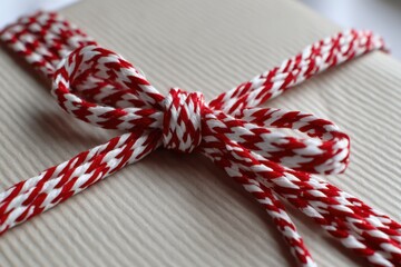 Beautifully wrapped gift with red and white string tied in a bow on textured paper surface