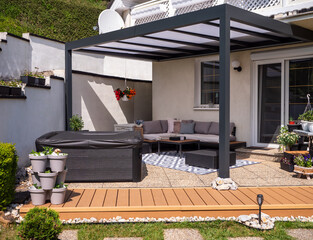 Aluminum patio terrace attached to a house with hot tub, sofa, plants, and coffee table on stone...