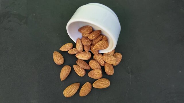 Falling almonds on black  background. Almond nuts fall on table. Close-up of brown almond nuts falling from white bowl on gray table. Pile of healthy food for vegan , cinematic badam 