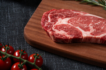 A fresh steak with rosemary, tomato, mushroom and garlic is placed on a wooden plate