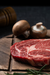 A fresh steak with rosemary, tomato, mushroom and garlic is placed on a wooden plate