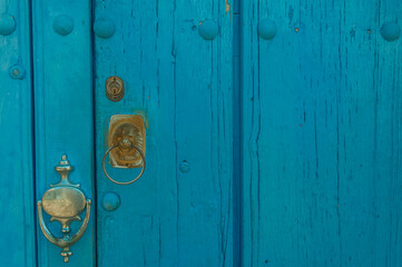 Weathered blue painted wooden door featuring a metal handle and knocker, showcasing a rustic and vintage architectural style