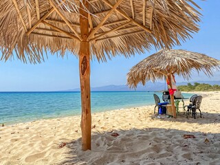 Straw beach umbrellas providing shade on a beautiful white sand beach in cuba, with turquoise water and mountains in the background