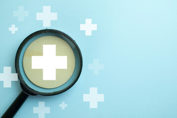 Magnifying glass focusing on a white medical cross over pastel blue background representing online...