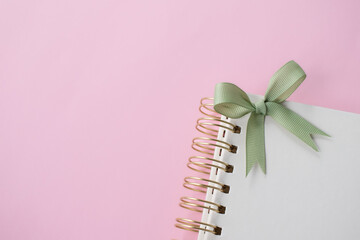 Notebook with a green ribbon bow on a pink background.