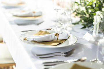 A wedding table covered with a white tablecloth, decorated with flowers, candles, glasses and cutlery