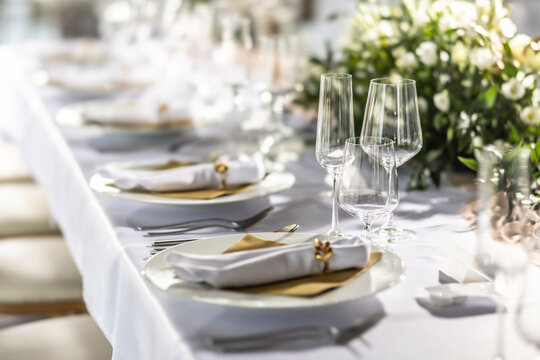 A wedding table covered with a white tablecloth, decorated with flowers, candles, glasses and cutlery