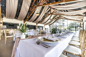 Wedding setting and decorated tables in a beautiful modern interior of a performance hall with a modern light ceiling of wooden construction