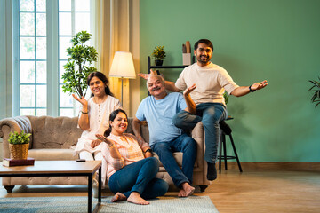 Laughing together while sitting indoors, cheerful Indian family enjoying quality time on sofa