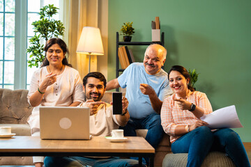 Happy Indian family seated on sofa indoors presenting smartphone screen with joyful expressions