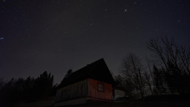 Lonely wooden house surrounded by trees under a starry night sky. Timelapse