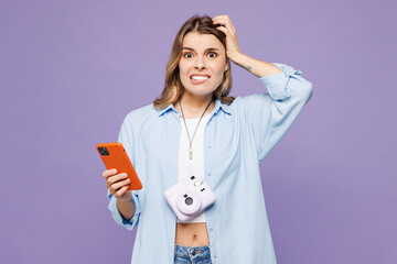 Traveler shocked woman wear blue clothes hold in hand use mobile cell phone isolated on plain...
