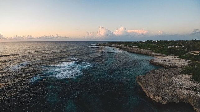 Serene sunset over a tropical coastline, featuring rocky shoreline, ocean waves, and lush vegetation.