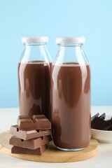 Tasty chocolate milk and pieces on white table against light blue background