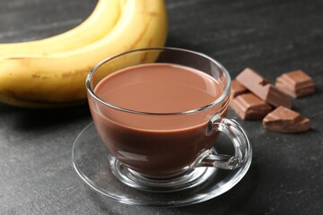 Tasty chocolate milk in glass cup, pieces and bananas on black table, closeup