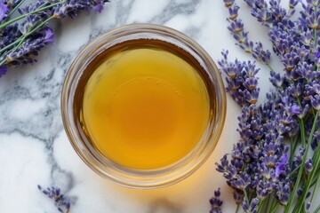 Fototapeta premium Overhead close up of golden honey in glass bowl with lavender sprigs on marble background for health and wellness