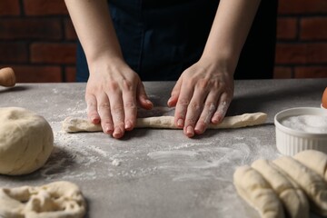 Woman making pretzel at light grey table, closeup