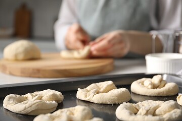 Woman shaping pretzels at table in kitchen, selective focus
