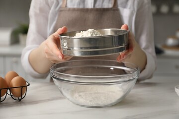 Making pretzels. Woman sieving flour in bowl at table indoors, closeup