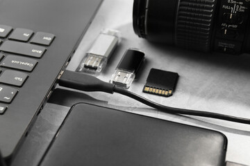 Flash drives, SD memory card, external hard disk, laptop and camera on gray textured table, closeup