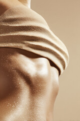 A close-up of a woman&rsquo;s torso with her top lifted to reveal her abdomen, the skin sprinkled with fine golden glitter that shimmers under soft, warm lighting against a neutral beige backdrop