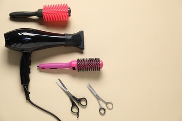 Round brushes, scissors and dryer on beige background, flat lay. Space for text