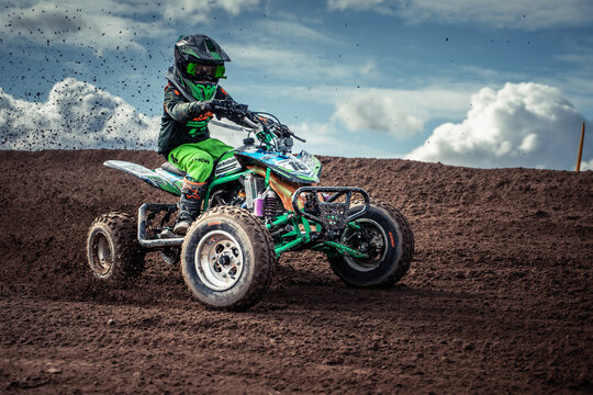 Latvia, Staicele, 26-04-2025  a person wearing a helmet, gloves, and goggles while riding a green and black ATV on top of a dirt field The sky in the background is filled with white, fluffy clo