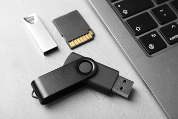 Flash drives, SD memory card and laptop on light grey table, closeup