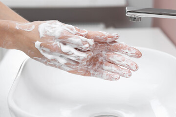 Woman washing hands at sink in bathroom, closeup