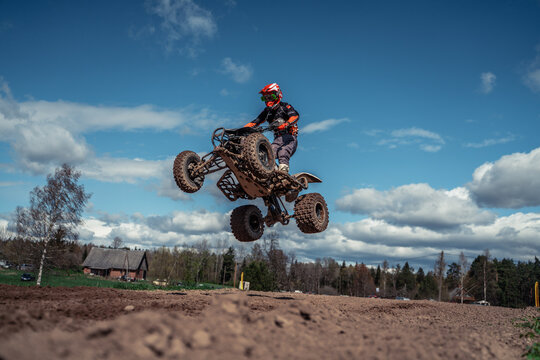 Latvia, Staicele, 26-04-2025  a person wearing a helmet and gloves riding a 2020 Can-Am Renegade X XC 1000R in Tyrone, Pennsylvania The ground is covered in soil and there are trees and houses