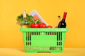 Shopping basket with different food products on yellow background