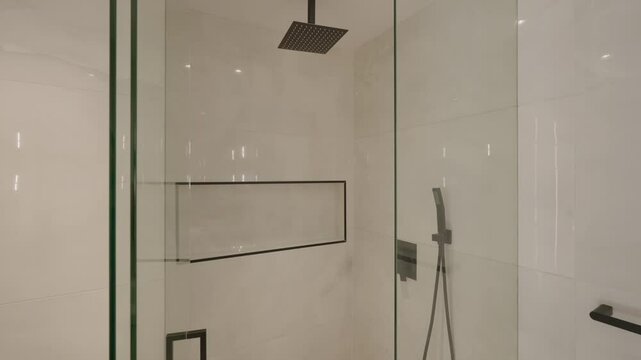 Glass shower enclosure with matte black fixtures and built in niche. Light colored tiles enhance spacious feel, creating elegant and modern bathroom design.