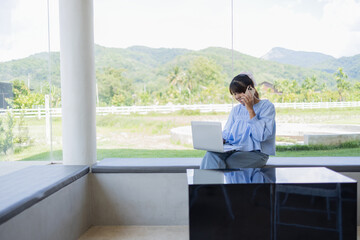 Fototapeta premium Digital nomad works happily in coffee shop using laptop and phone with scenic mountain view in background for business in relaxed setting