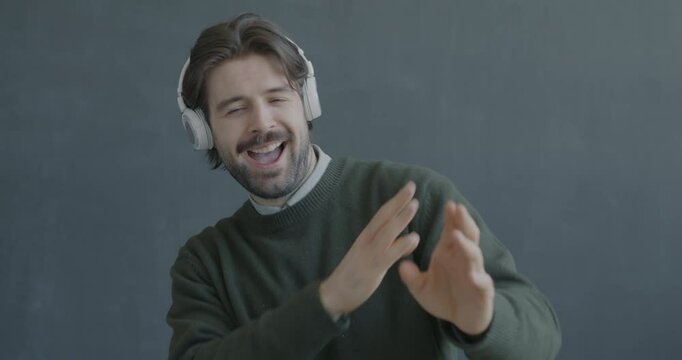 Slow motion portrait of joyful young man listening to music through headphones dancing on black background. People and youth culture concept.